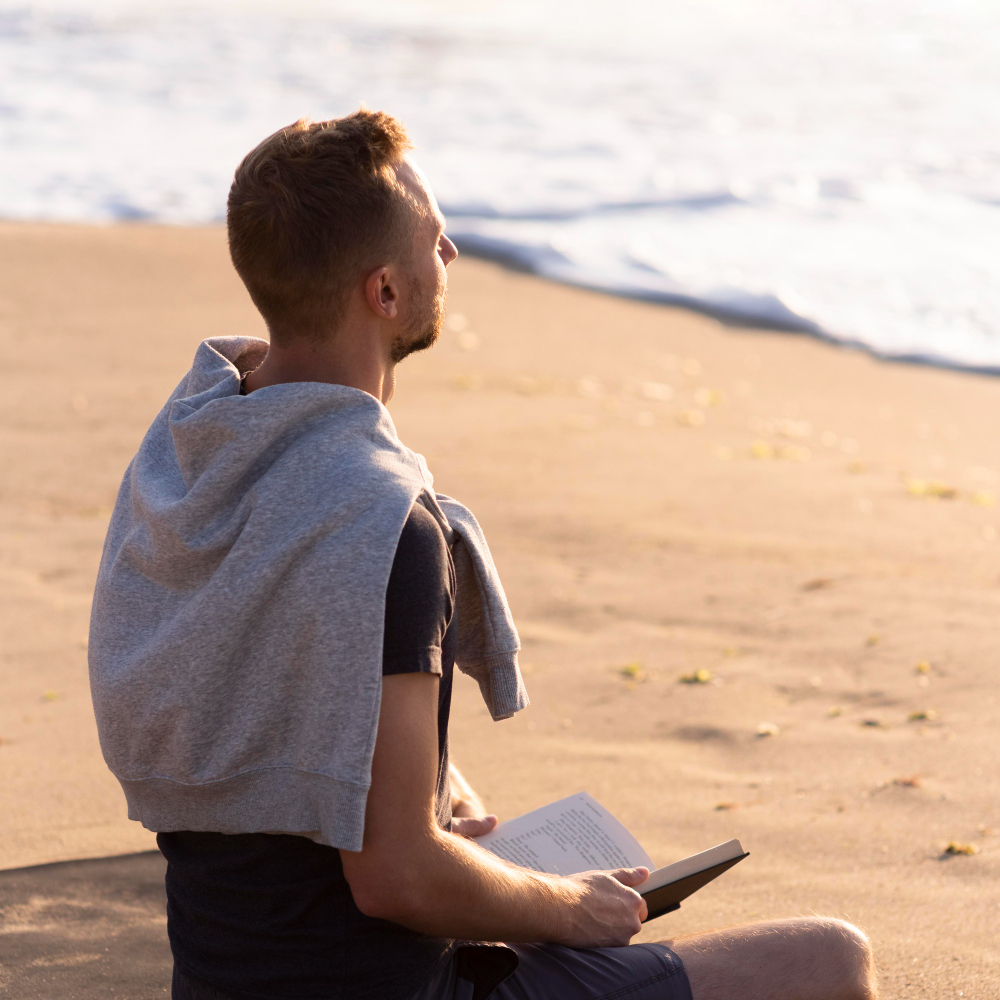 Homme méditant au bord de la mer, un livre ouvert entre les mains.